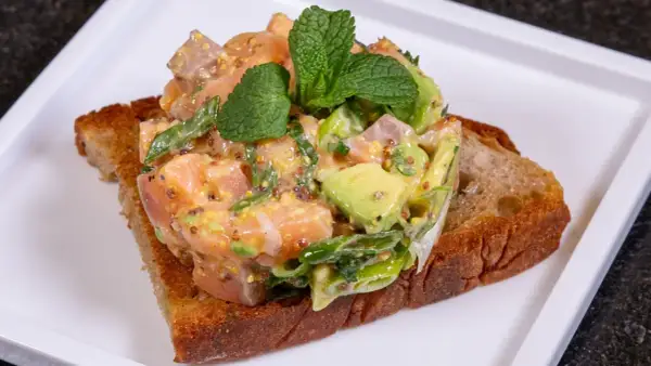 Lachs-Tatar mit Avocado auf geröstetem Brot, garniert mit Minze. Ein Gericht, das selbst Sterneköche begeistert.