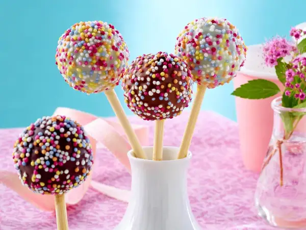 Bunte cake pops mit Schokoglasur und Streuseln in einer weißen Vase, bereit für eine fröhliche Feier.