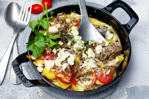Herzhaft gebackener Feta mit Hackfleisch, Kartoffeln und Tomaten in einer schwarzen Gusseisenpfanne, garniert mit frischer Petersilie.