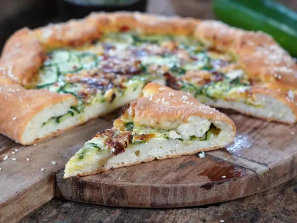 Eine köstliche Zucchini-Pizza mit goldbraunem Teig und saftiger Füllung, auf einem rustikalen Holzbrett serviert.