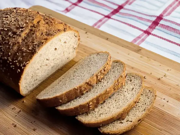 Ein frisch gebackenes Brot, perfekt für ein keto brot rezept, liegt auf einem Holzbrett. Mehrere Scheiben sind bereits abgeschnitten.
