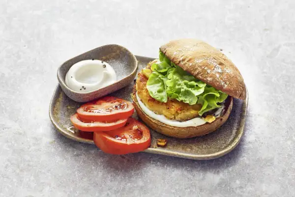 Ein saftiger vegetarischer Burger mit knackigem Salat, dazu frische Tomatenscheiben und eine cremige Sauce. Ein Genuss für alle Sinne!
