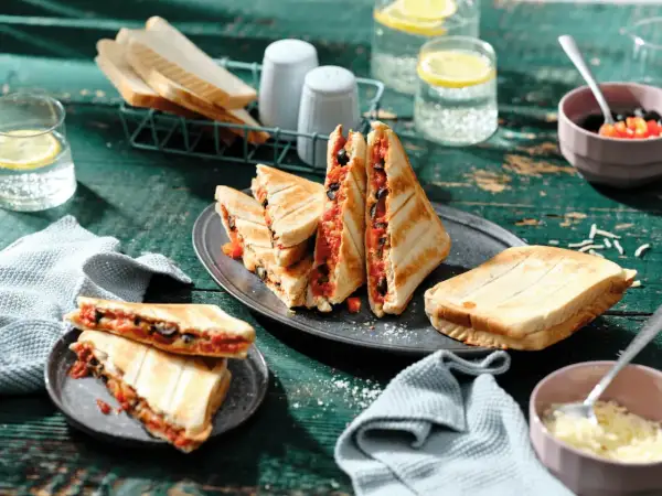 Leckere Sandwichmaker Rezepte: Getoastete Sandwiches mit Tomaten und Oliven, serviert mit Zitrone-Wasser.