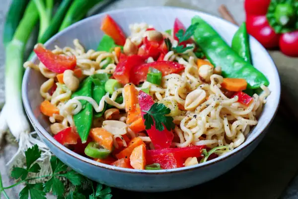 Bunter mie nudel salat mit Erdnüssen, Paprika, Zuckerschoten und Karotten, garniert mit Petersilie.