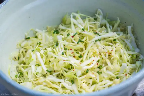 Frischer Spitzkohl Salat, fein geschnitten und mit Schnittlauch und Chiliflocken garniert, wartet in einer Schüssel.