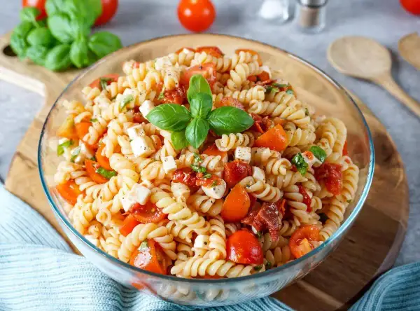 Ein köstlicher mediterraner Nudelsalat mit Fusilli, Kirschtomaten, Mozzarella und frischem Basilikum, garniert mit einem Basilikumblatt.